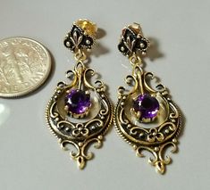 Pair of marked 14K yellow gold drop and dangle style vintage pierced earrings, with a post and friction fit back for fastening. Each earring is set with one round faceted beautiful purple amethyst gemstone. Each amethyst measures approximately 6.00 mm x 6.00 mm. Each amethyst is attached to a moveable design in the center of each earring. The pair of 14K yellow gold amethyst earrings are accented with black enamel, highlighting the 14K yellow  gold scroll design and amethyst beautifully. The pair of 14K yellow gold amethyst earrings weigh 5.90 grams. The pair of earrings are in excellent condition. The pair of earrings come in a quality earring box. The earrings were identified, tested and described by a Graduate Gemologist, GIA. Regal Earrings, Odd Jewelry, Aquarius Quotes, Jewelry Making Earrings, Garnet Earrings, Scroll Design, Wire Weaving, Antique Earrings, Sapphire Earrings