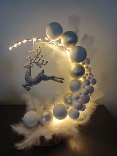 a white and silver christmas decoration with lights on the top is surrounded by balls and feathers