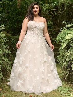 a woman wearing a wedding dress standing in the woods with her hands on her hips