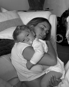 a woman holding a baby in her arms while laying on top of a bed next to pillows