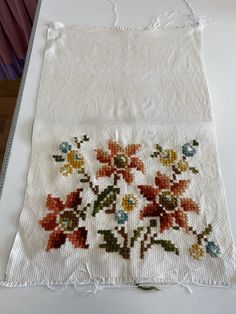 an embroidered piece of cloth with flowers on the side and fringe around it, sitting on a table