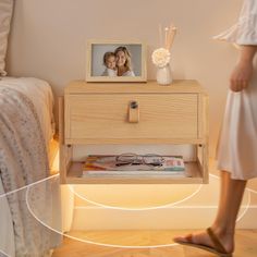 a woman standing next to a bed with a wooden night stand on top of it