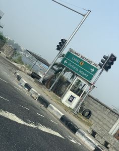 a traffic light sitting next to a street sign on the side of a road in front of a cement wall