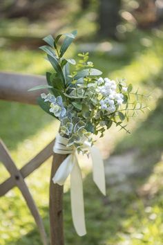 a bouquet of white flowers tied to a wooden fence post with greenery in the background