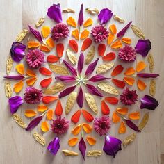 a circular arrangement of colorful flowers on a wooden surface with gold leaves and petals arranged in the center