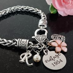 Celebrate her milestone birthday with this thoughtful 'vintage 1954' 70th birthday gift. The bracelet features a 'vintage 1954' laser engraved stainless steel charm, flower, filigree heart, cream pearl, and a script initial for personalization. It comes beautifully packaged and ready to gift.  *'Vintage 1955' is now available for those celebrating their 70th birthday in year 2025. You can select the vintage year charm needed in the drop down box when ordering. Seventieth birthday gift for Wife, Classic Stainless Steel Name Bracelet For Anniversary, Metal Charm Bracelet For Anniversary, Classic Silver Name Bracelet For Birthday, Classic Engraved Bracelets For Birthday, Engraved Bracelet For Anniversary, Silver Charm Bracelet For Anniversary, Classic Adjustable Charm Bracelet For Anniversary, Classic Engraved Charm Bracelet For Anniversary, Classic Personalized Charm Bracelet For Anniversary