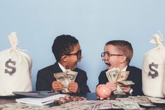 two young boys sitting at a table with money and piggy bank in front of them