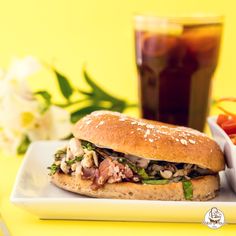 a sandwich with meat and vegetables on a plate next to a glass of soda,