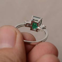 a person is holding a ring with a green stone on the top and bottom part