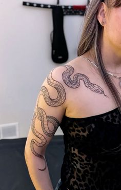 a woman with a snake tattoo on her arm and shoulder, standing in front of a wall