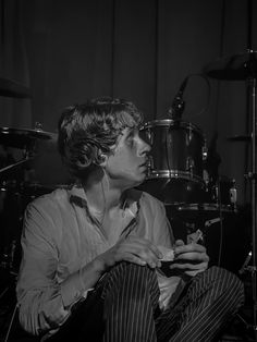 a man sitting in front of a drum set with his hands on his chest and looking at something