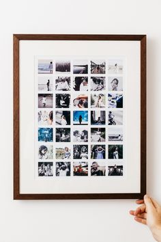 a person holding up a framed photo with multiple photos on it in front of a white wall