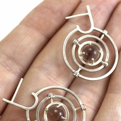 Manufactured entirely by hand from sterling silver wire, featuring two 7mm natural quartz spheres, the armillary hoops rotate on two axes. Each earring is individually and arduously calibrated for symmetry. Easily a wardrobe staple, there are numerous ways to arrange the two layers of kinetic concentric circles. Measuring a little under 1 inch across and a little over an inch long, these marvels make themselves known while remaining light on the lobe. Concentric Circles, Natural Rock, Quartz Sphere, Rock Crystal, Axes, Silver Wire, Wardrobe Staples, Circles, 1 Inch