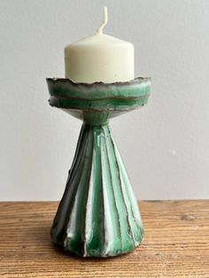 a small green and white candle holder sitting on top of a wooden table