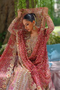 a woman in a red and gold bridal gown sitting on a bench under a tree