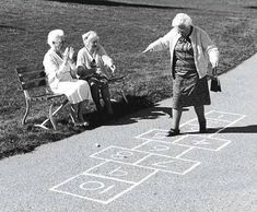 an old woman is playing hopo game with two older women on the sidewalk in front of her