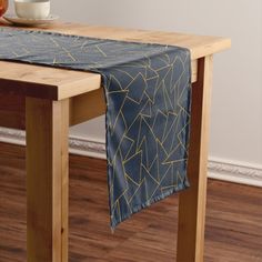 a wooden table topped with a blue and yellow table runner next to a bowl of fruit