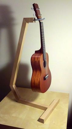 a wooden guitar stand with an acoustic instrument on it's back and neck, in front of a white wall