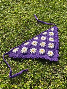 a purple crocheted bag with white flowers on it laying in the green grass