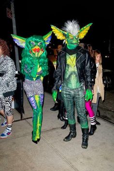 two people dressed in costumes walking down the street at night with other people standing around