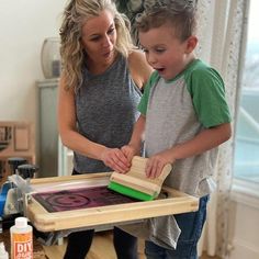 a woman standing next to a little boy with a wooden block on top of it