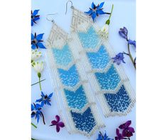 two blue and white earrings with flowers in the background on a table next to it