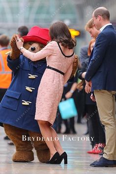 a woman in a pink dress hugging a teddy bear on the street with other people behind her