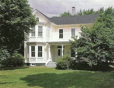 a large white house sitting in the middle of a lush green field next to trees