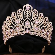 a tiara with pink stones on it sitting on top of a black cloth covered table