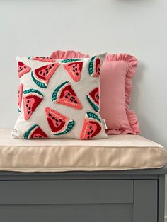 a watermelon pillow sitting on top of a bench next to a pink pillow