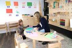 a woman and child sitting at a table in a room with wooden shelves on the wall