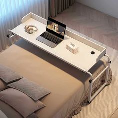 a laptop computer sitting on top of a white desk next to a bed with pillows