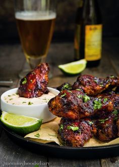 chicken wings with dipping sauce and lime wedges on a plate next to a glass of beer