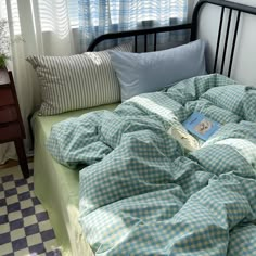 an unmade bed with blue and white checkered sheets, pillows and a book on it