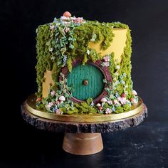 a cake decorated with moss and flowers on top of a wooden stand in front of a black background