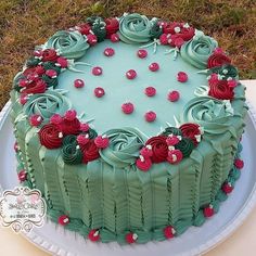 a green cake with red roses on it sitting on a white plate in the grass