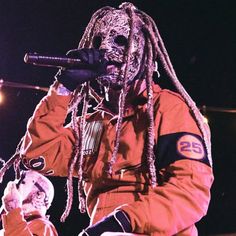 a man with dreadlocks holding a microphone in his hand and wearing an orange jacket