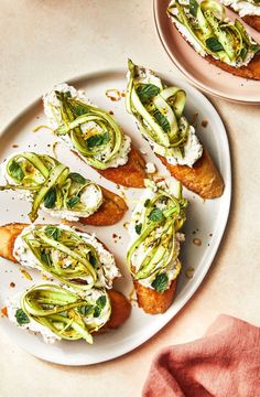 several pieces of bread topped with cucumbers and cream cheese on top of a white plate