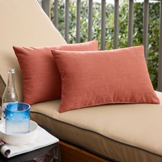 two orange pillows sitting on top of a couch next to a cup and water bottle