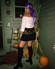 a woman with purple hair and black boots standing in front of a house next to pumpkins