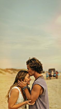 a man and woman standing on top of a sandy beach next to the ocean kissing