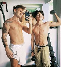 two shirtless men standing in front of a mirror taking a selfie with their cell phone