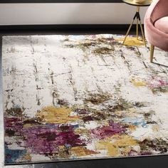 an area rug with colorful paint splattered on it and a pink chair in the background