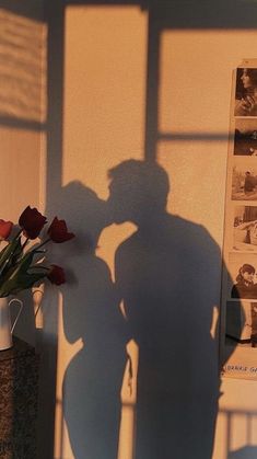 the shadow of a person standing next to a vase with flowers in it