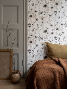 a bed sitting next to a wall with a flower pattern on the wall and pillows