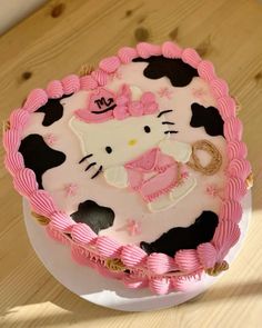 a hello kitty birthday cake with pink and black icing on a wooden table top