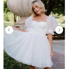 a woman in a short white dress standing next to a fountain