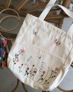 a white bag with flowers and butterflies on it sitting on a chair next to some scissors