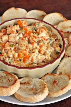 a white plate topped with crackers and a bowl filled with dip surrounded by bread