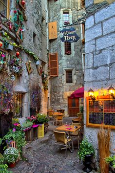 an old stone building with flowers growing out of it's windows and tables in the courtyard